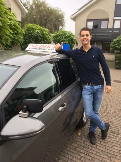 Leerling van Autorijschool Sediki bij de lesauto na een geslaagd rijexamen
