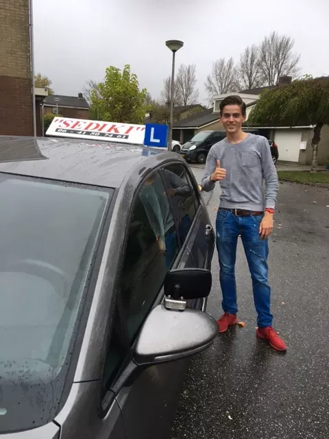 Leerling met duim omhoog naast de lesauto van Autorijschool Sediki