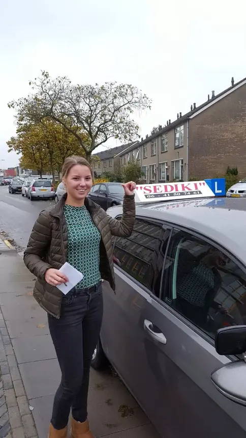 Geslaagde leerling met haar rijbewijspapieren naast de lesauto van Sediki