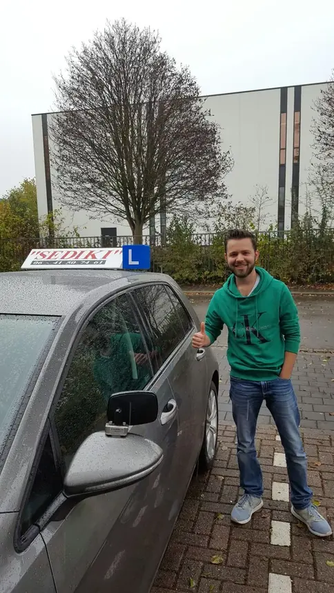 Geslaagde leerling met duim omhoog naast de lesauto van Autorijschool Sediki