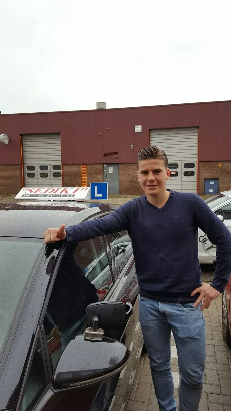 Leerling leunt tegen de lesauto van Autorijschool Sediki na het rijexamen