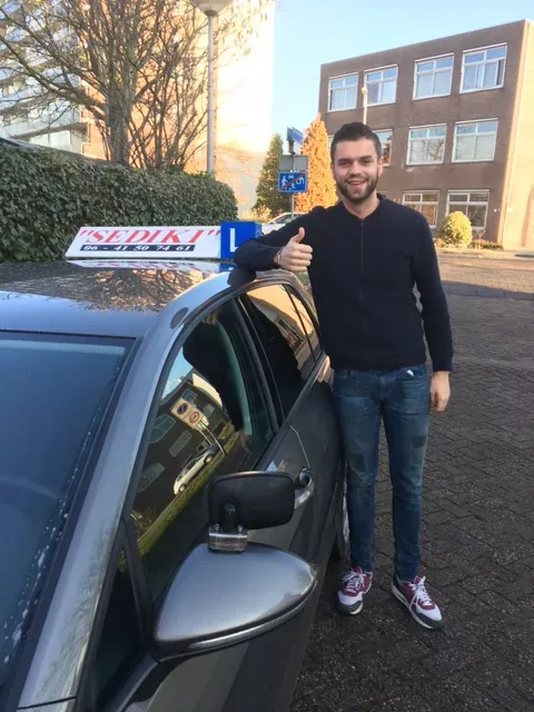 Geslaagde leerling met duim omhoog voor de lesauto van Autorijschool Sediki